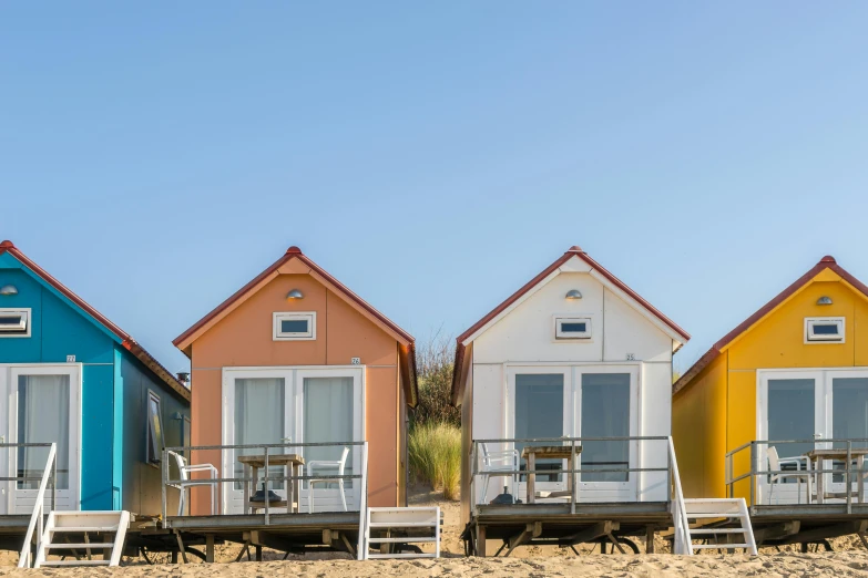 a row of beach huts sitting on top of a sandy beach, a portrait, by Matthias Stom, unsplash, renaissance, tiny house, three views, halogen, yellow and orange color scheme