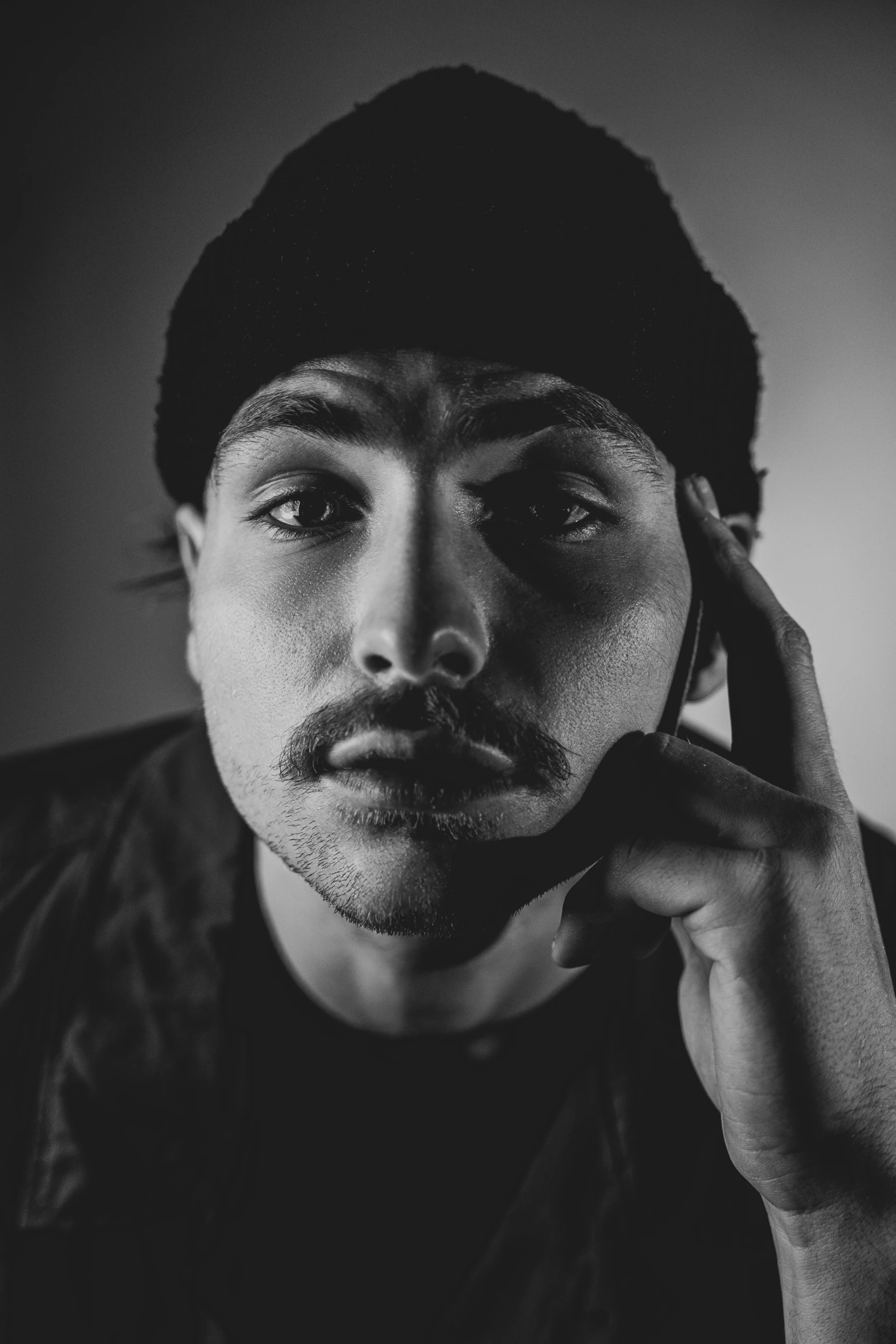 a black and white photo of a man talking on a cell phone, a black and white photo, inspired by Camilo Egas, pexels contest winner, hyperrealism, wearing a beanie, mustache and soul patch, frank dillane as puck, portait photo profile picture