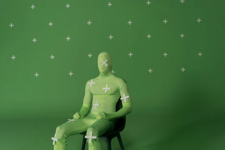 a mannequin sitting on a chair in front of a green background, inspired by Edmond Xavier Kapp, laserpunk fullbodysuit, sitting cross-legged, twinmotion render, covered in bandages