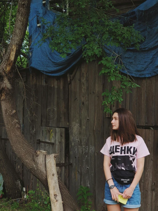 a woman standing in front of a wooden fence, a picture, by Attila Meszlenyi, wearing a t-shirt, ((pink)), ukraine. photography, on a tree