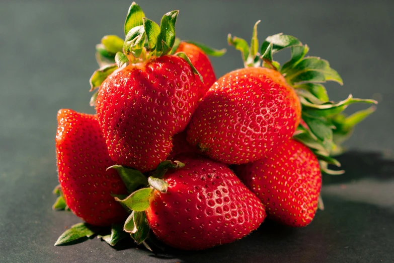 a bunch of strawberries sitting on top of a table, against dark background, detailed product image, highly upvoted, looking towards camera