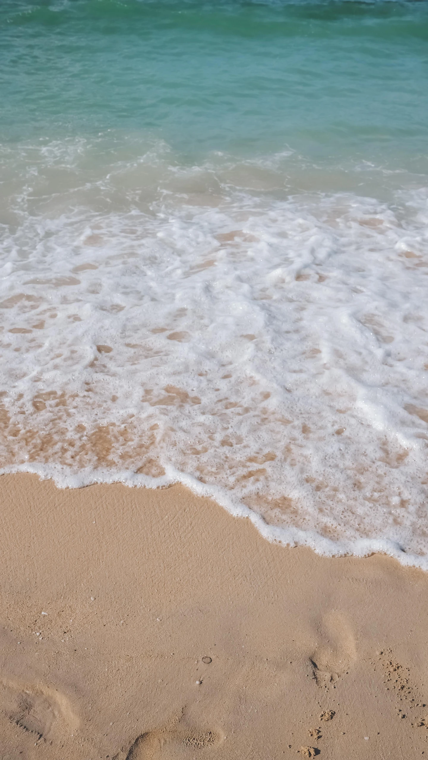 a surfboard sitting on top of a sandy beach, there is water splash, beach on the outer rim, up close, the ocean