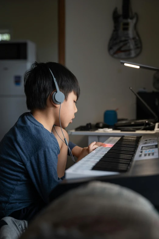 a little boy that is sitting in front of a keyboard, wearing black headphones, darren quach, lit from the side, at home