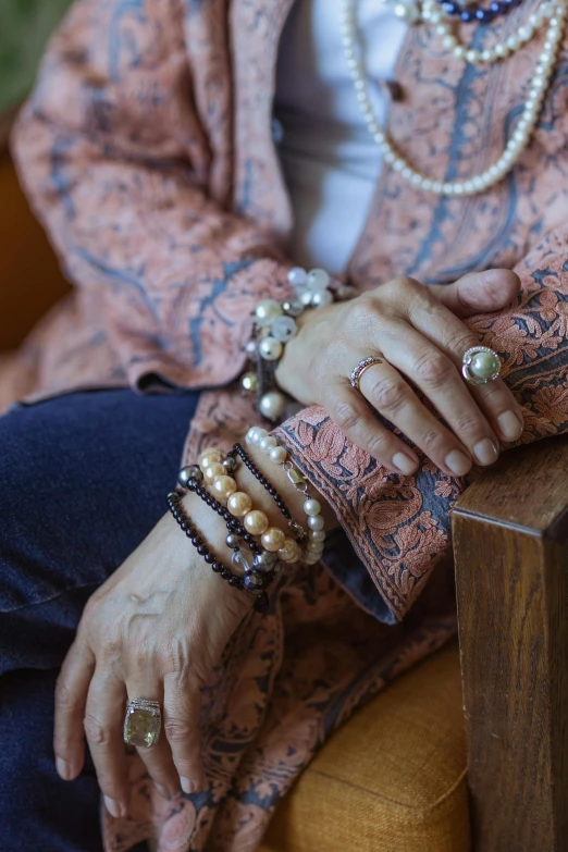 a close up of a person sitting on a chair, by Nina Hamnett, renaissance, bracelets and necklaces, older woman, pearls, patterned clothing