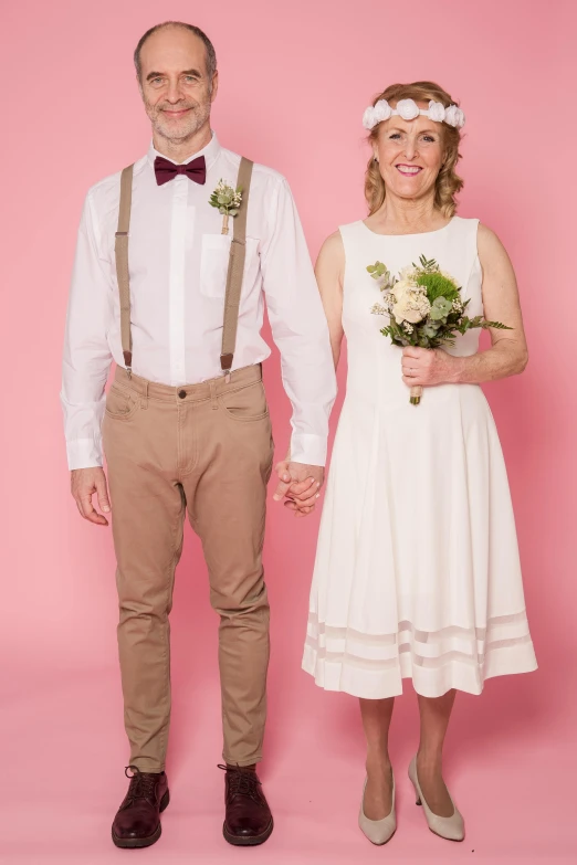 a man and a woman standing next to each other, a colorized photo, by Lee Loughridge, pexels, white and pink, groom, short person, solid color backdrop