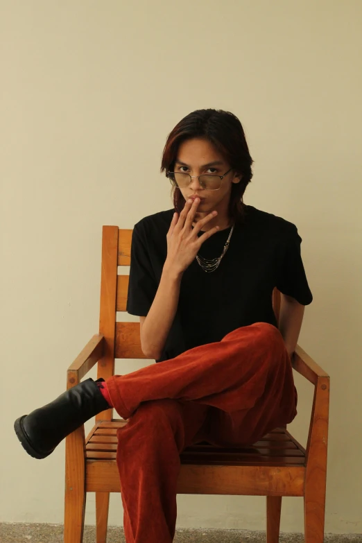 a woman sitting on top of a wooden chair, by Pablo Rey, trending on unsplash, visual art, he is smoking a cigarette, androgynous person, red shirt brown pants, wearing small round glasses