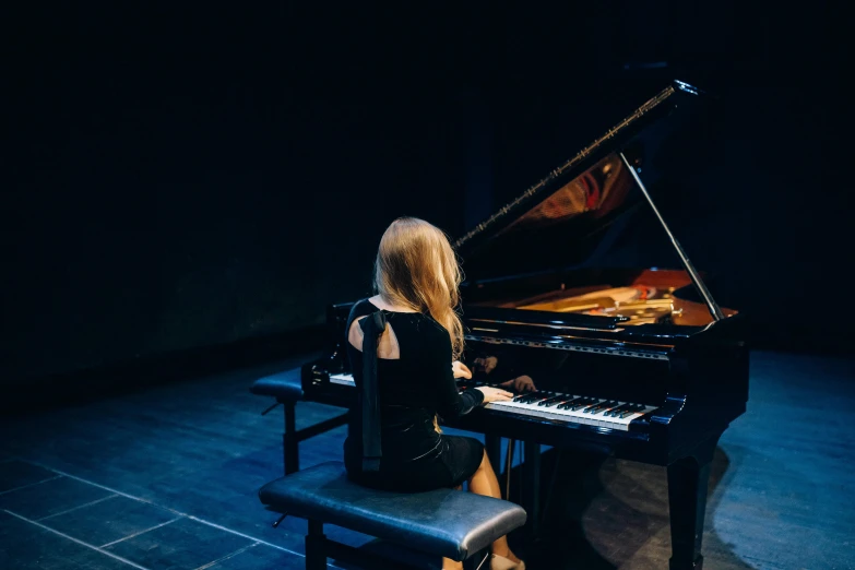 a woman sitting at a piano in a dark room, by Julia Pishtar, unsplash, performing on stage, plain background, multiple stories, dmitry bogdanov