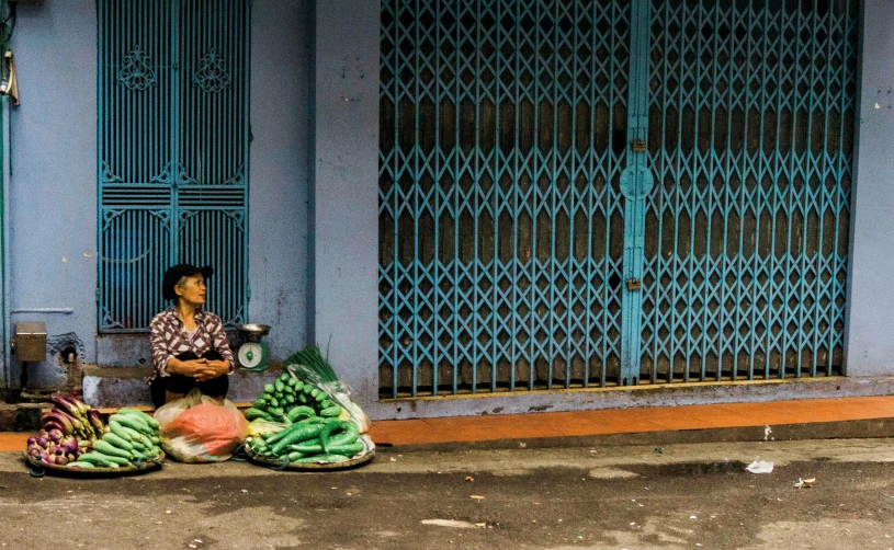 a woman sitting in front of a blue building, pexels contest winner, cloisonnism, wet market street, greens and blues, square, waiting to strike