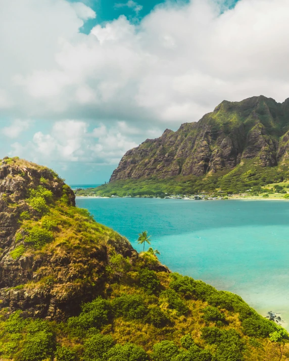 a large body of water sitting on top of a lush green hillside, pexels contest winner, polynesian style, craggy mountains, overlooking the beach, listing image