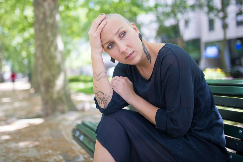 a woman with a bald head sitting on a bench, devastated, looking towards camera, tumours, portrait image