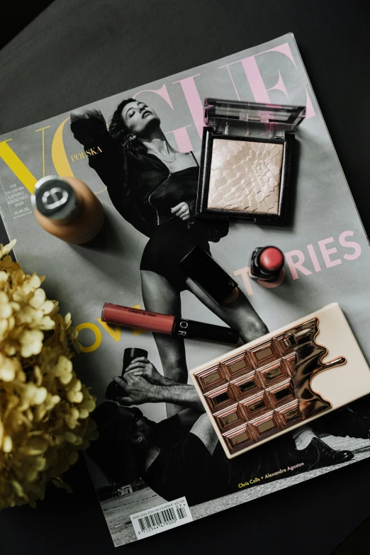 a magazine sitting on top of a table next to a flower, a picture, by Julia Pishtar, pexels contest winner, lots of makeup, chocolate. rugged, chanel, brunette