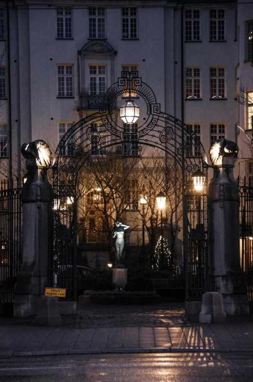 a building that is lit up at night, a statue, inspired by Heinrich Danioth, iron gate, cosy atmoshpere, gas lanterns, school courtyard