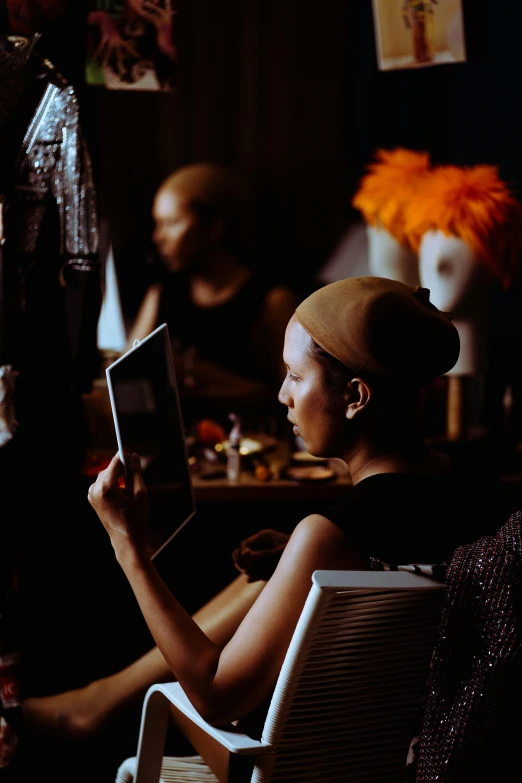 a woman sitting in a chair reading a book, a portrait, inspired by Georges de La Tour, unsplash, fashion week backstage, afrofuturism style, using a magical tablet, photo taken on fujifilm superia