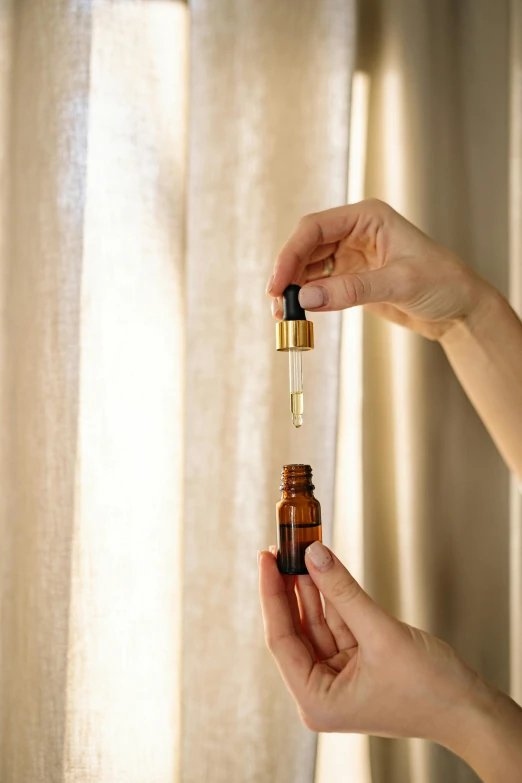 a close up of a person holding a bottle of oil, ambient amber light, the window is open, vibrant vials, manuka