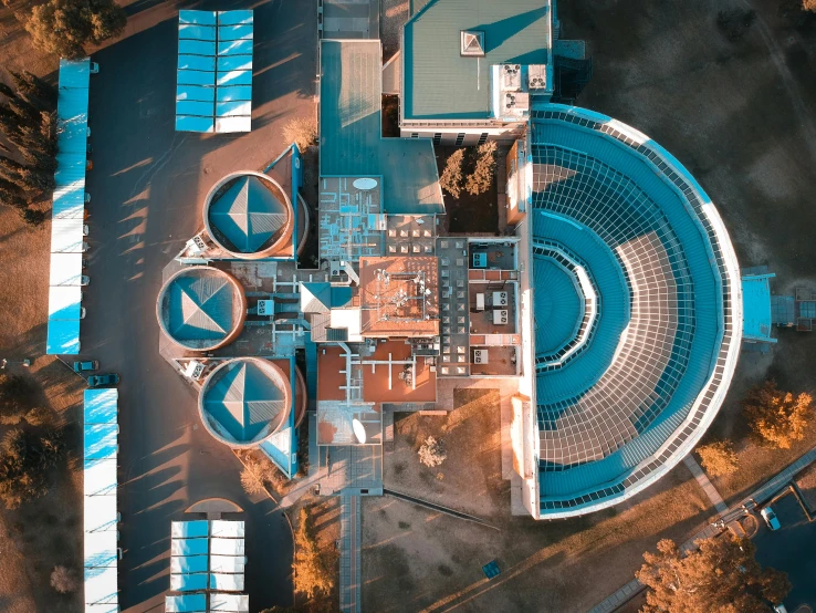 an aerial view of a building surrounded by trees, by Adam Marczyński, pexels contest winner, photorealism, metal towers and sewers, inside a science facility, rounded roof, cyan