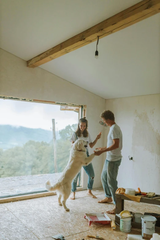 a man and a woman playing with a dog, by Arabella Rankin, pexels contest winner, passive house, plaster, inside of a cabin, ( dog ) jumps from mountain