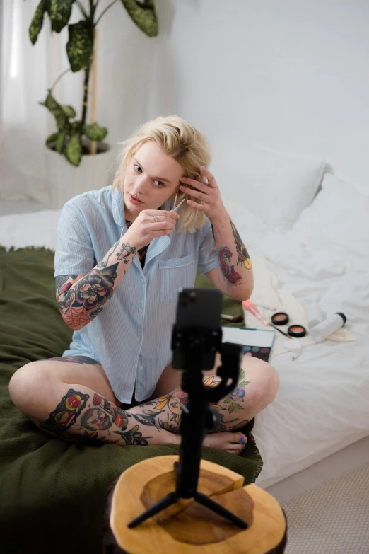 a woman sitting on a bed talking on a cell phone, a tattoo, trending on pexels, holding a camera, blond, webcam, avatar image