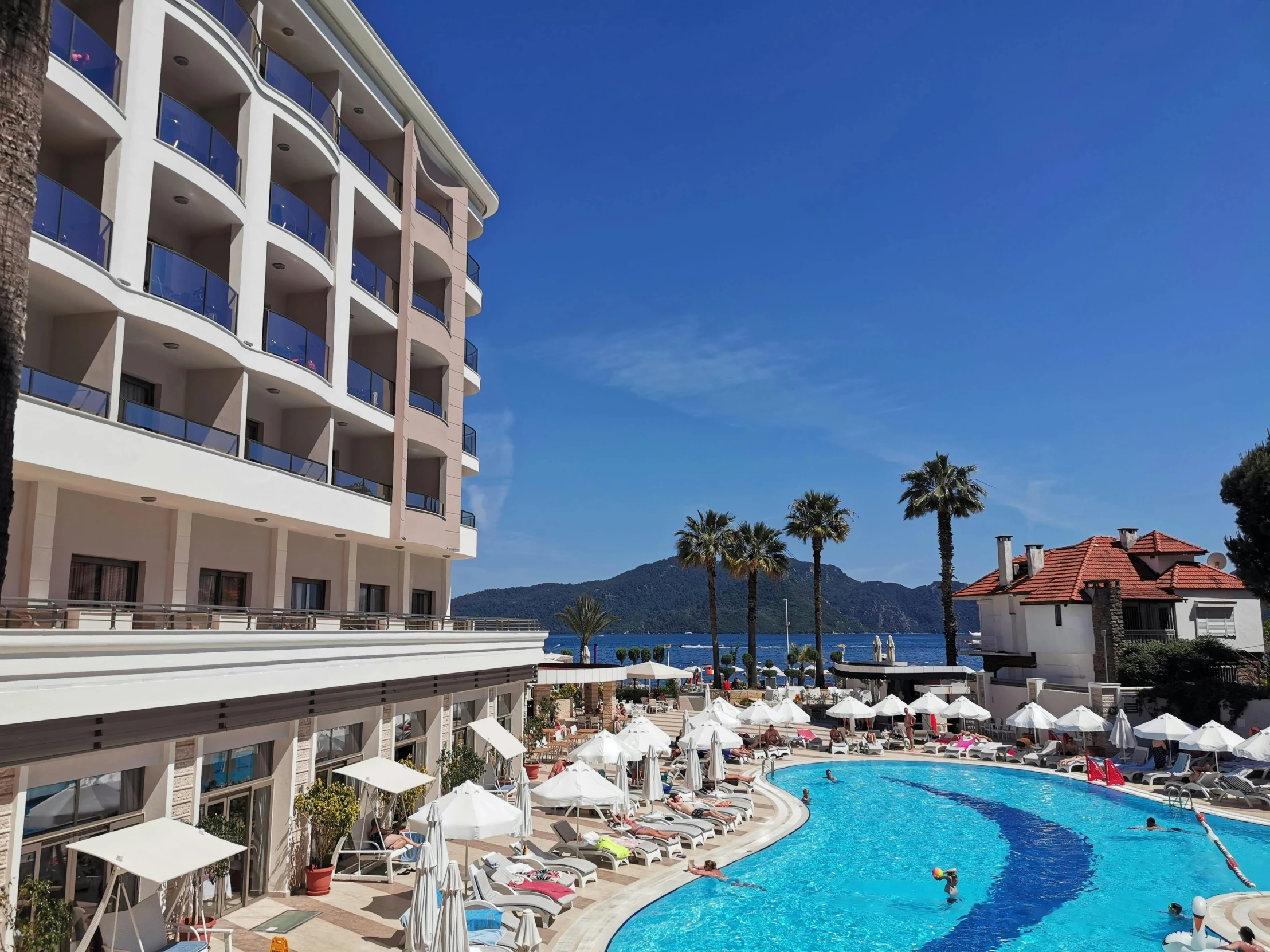 an outdoor swimming pool with lounge chairs and umbrellas, art nouveau, white marble buildings, in a beachfront environment, profile image, turkey