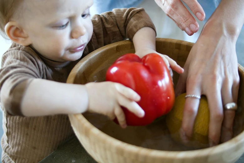 a baby playing with a red pepper in a bowl, pexels, process art, caring fatherly wide forehead, sink, a wooden, red and yellow scheme