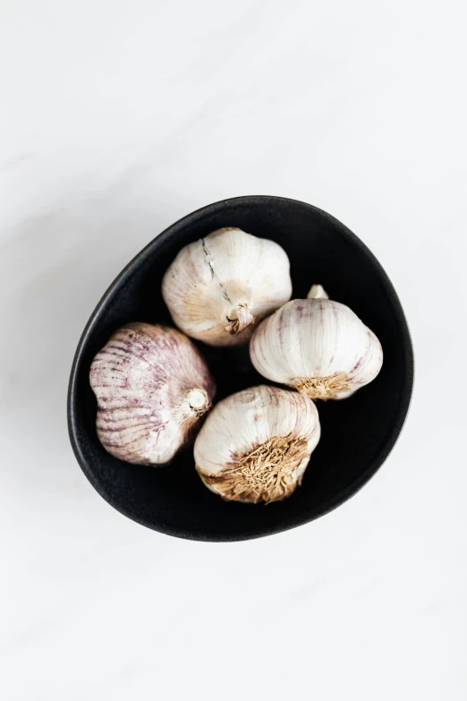 a black bowl filled with garlic on top of a white table, westside, 3 - piece, silver haired, full product shot