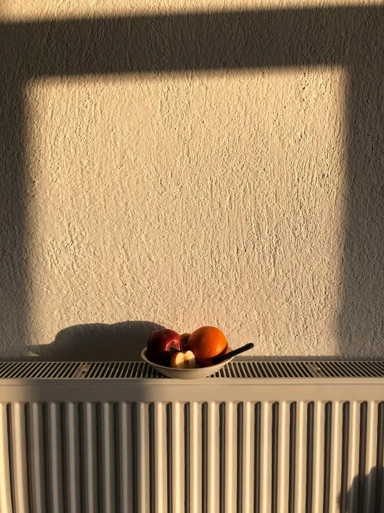 a bowl of fruit sitting on top of a radiator, inspired by Georg Schrimpf, postminimalism, ((sunset)), taken on iphone 14 pro, low quality photo, natural light outside
