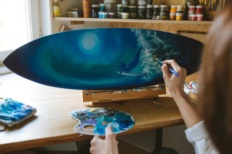 a woman is painting a surfboard on a table, an airbrush painting, by Julia Pishtar, pexels contest winner, moon light fish eye illustrator, canvas art print