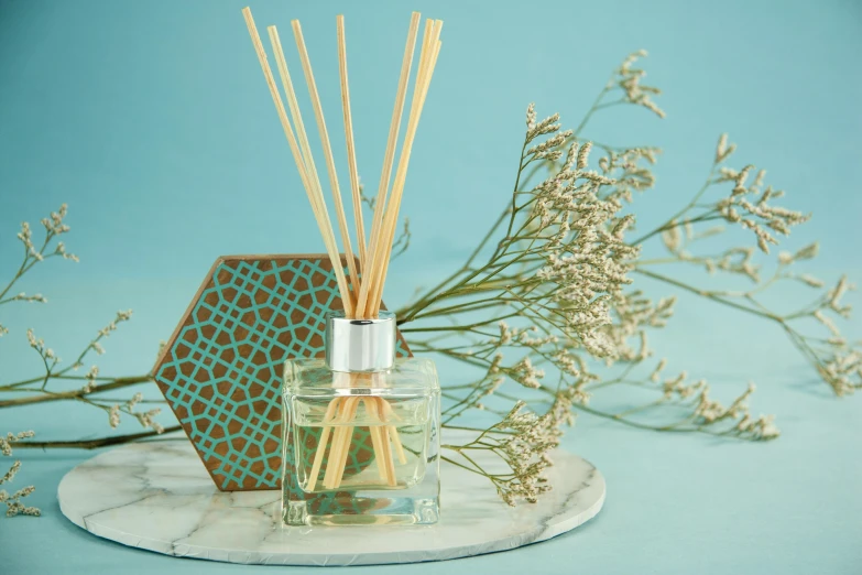 a bottle of perfume sitting next to a bunch of flowers, inspired by Eden Box, arabesque, relaxed. blue background, reeds, hexagonal shaped, at home