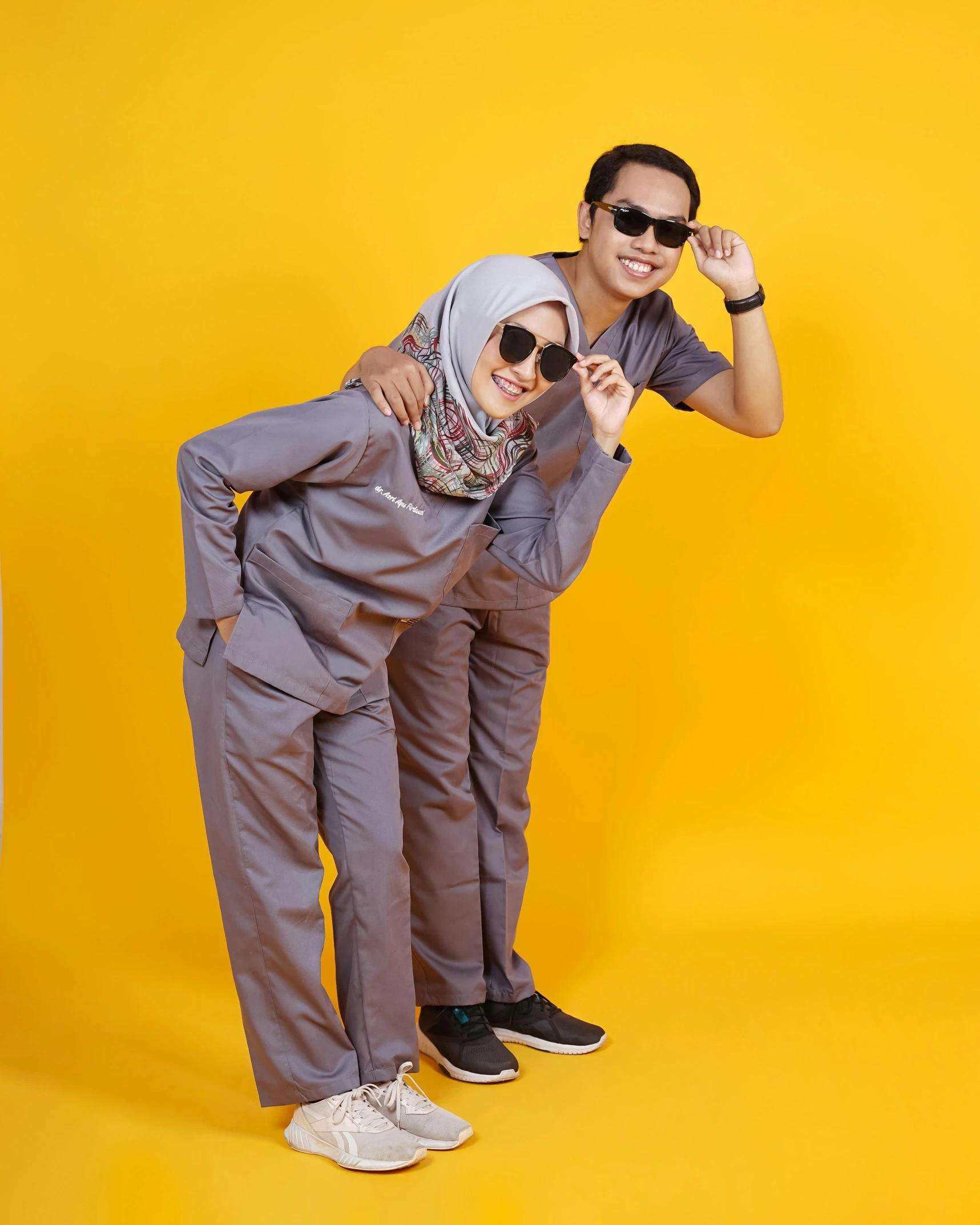 a man and a woman standing next to each other, by Basuki Abdullah, wearing human air force jumpsuit, grey skin, nurse scrubs, playful pose