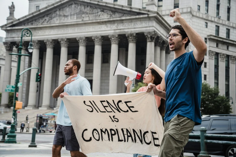 a group of people holding a sign in front of a building, shutterstock, renaissance, justice, silence, attacking nyc, i és complex