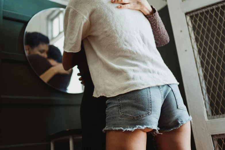 a woman hugging a man in front of a mirror, by Nina Hamnett, trending on pexels, denim short pants, view from back, lesbian embrace, round thighs