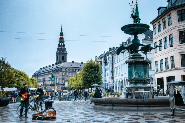 a group of people walking down a street next to a fountain, a statue, by Jesper Knudsen, pexels contest winner, denmark, square, city panorama, a green