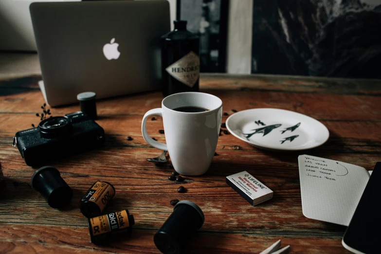 a coffee cup sitting on top of a wooden table, a still life, inspired by Arnold Newman, pexels contest winner, with a bunch of stuff, computer wallpaper, strange ingredients on the table, lo-fi