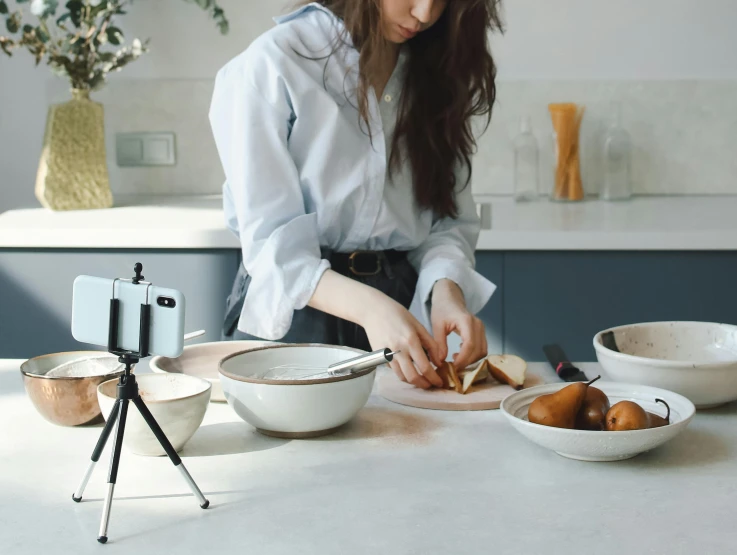 a woman is preparing food in a kitchen, a still life, inspired by Yukimasa Ida, trending on pexels, video art, tripod, smartphone photo, standing elegantly, on a white table