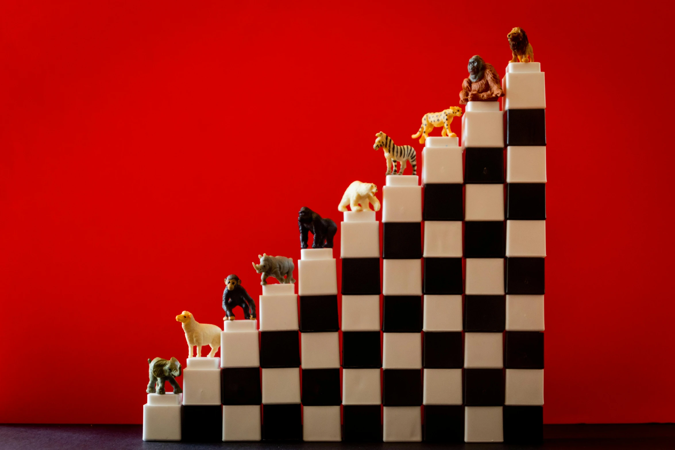 a group of figurines sitting on top of a black and white cake, by Adam Marczyński, unsplash, op art, on a red background, animals wildlife, stairway to heaven, board games on a table