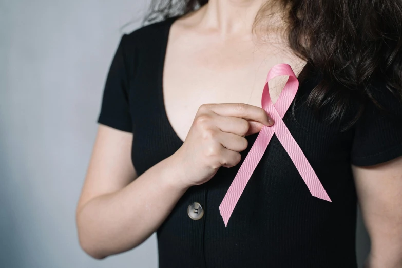 a close up of a person holding a pink ribbon, trending on pexels, she is wearing a black tank top, medical image, ilustration, conservatively dressed