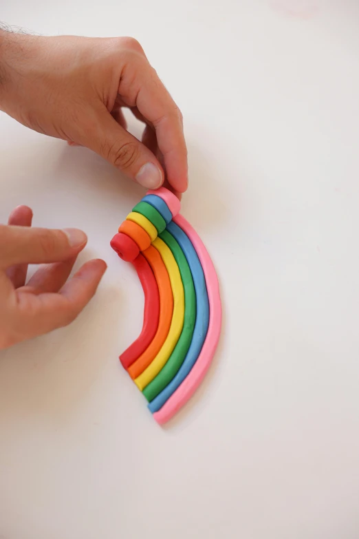 a close up of a person playing with a toy, sitting on top of a rainbow, made out of clay, showing curves, assembly instructions