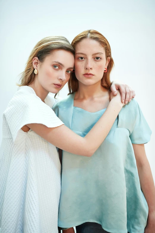 a couple of women standing next to each other, pale blue outfit, photoshoot for skincare brand, arm around her neck, pale cyan and grey fabric