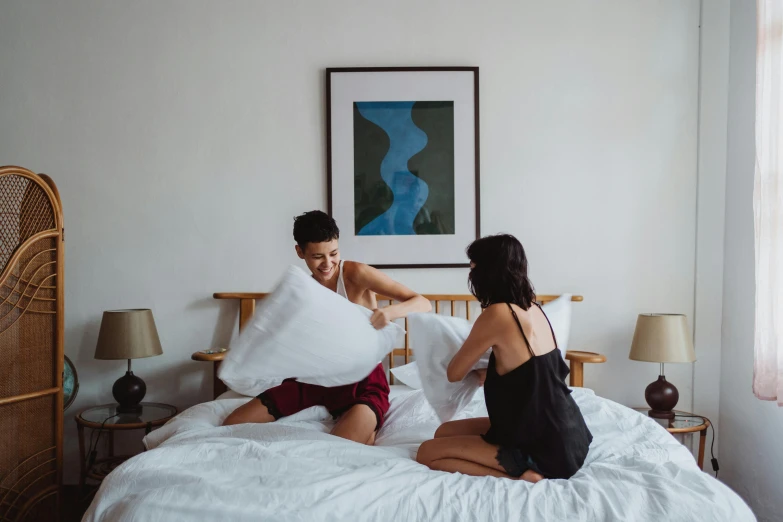 a couple of people that are sitting on a bed, by Julia Pishtar, pexels contest winner, lesbian, maintenance, pillows, excited