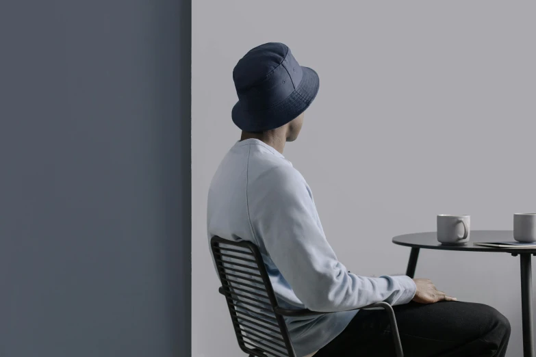 a person sitting at a table with a cup of coffee, dark blue beanie, sitting on designer chair, bucket hat, human computer