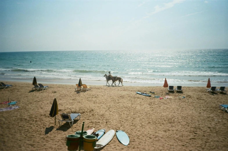 a person riding a horse on top of a sandy beach, a polaroid photo, unsplash, plasticien, standing on surfboards, israel, 2000s photo