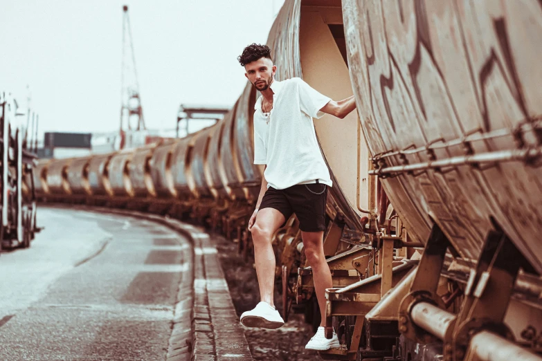 a man standing on the side of a train, pexels contest winner, bra and shorts streetwear, trendy white clothing, photoshoot for skincare brand, liam brazier