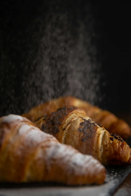 a couple of croissants sitting on top of a counter, a portrait, by Tom Bonson, trending on unsplash, flour dust flying, close up shot from the side, woodfired, shot with sony alpha 1 camera