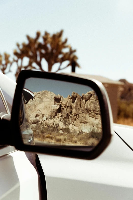 a side view mirror on the side of a white car, unsplash, photorealism, rock formations, conde nast traveler photo, photographed from behind, desert setting