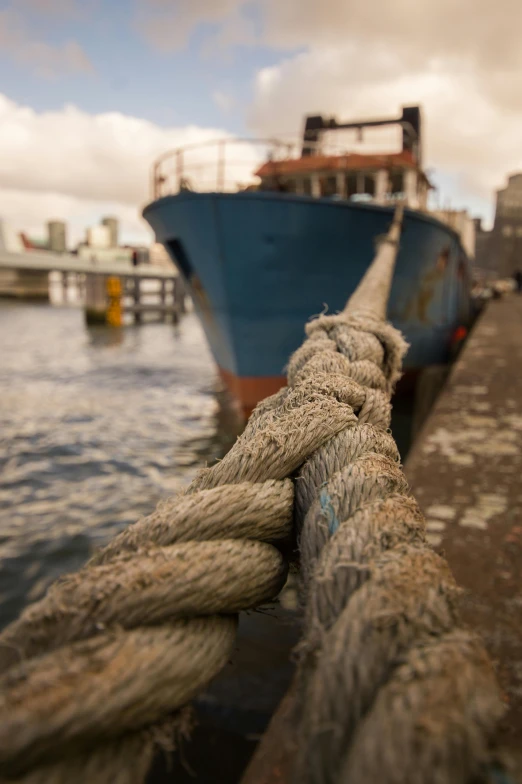 a close up of a rope with a boat in the background, by Dan Scott, urban surroundings, ships, brown, malika favre