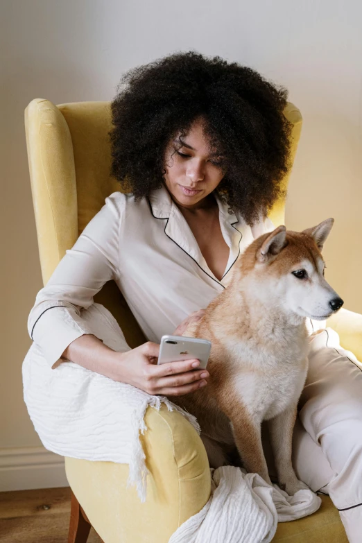 a woman sitting in a chair with a dog, a stock photo, trending on pexels, renaissance, checking her phone, shibu inu, grey, tan