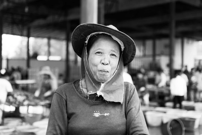 a black and white photo of a woman wearing a hat, a black and white photo, vietnamese woman, grimacing, elderly woman, having a snack