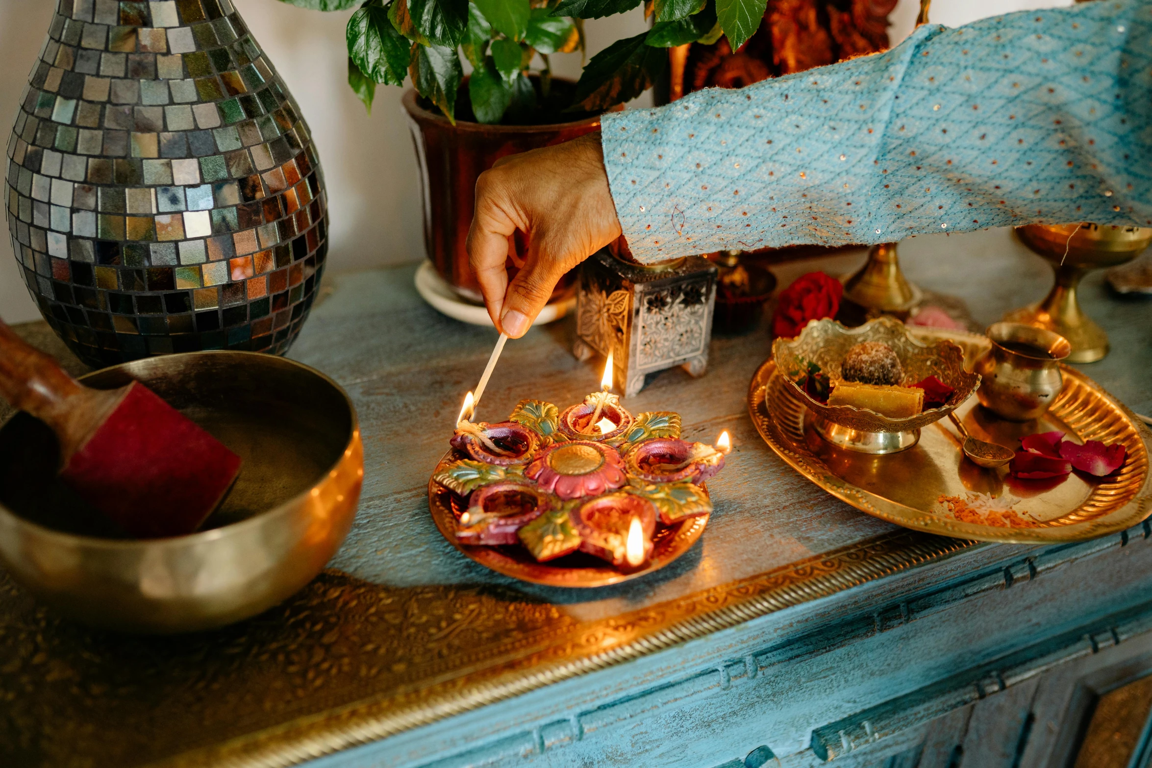 a person lighting a candle on a table, hurufiyya, multicoloured, bollywood, cyan and gold scheme, snacks