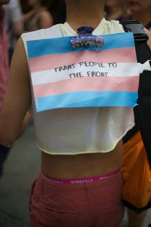 a woman walking down a street with a sign on her back, happening, trans rights, wearing tanktop, pink and blue colors, viewed from below