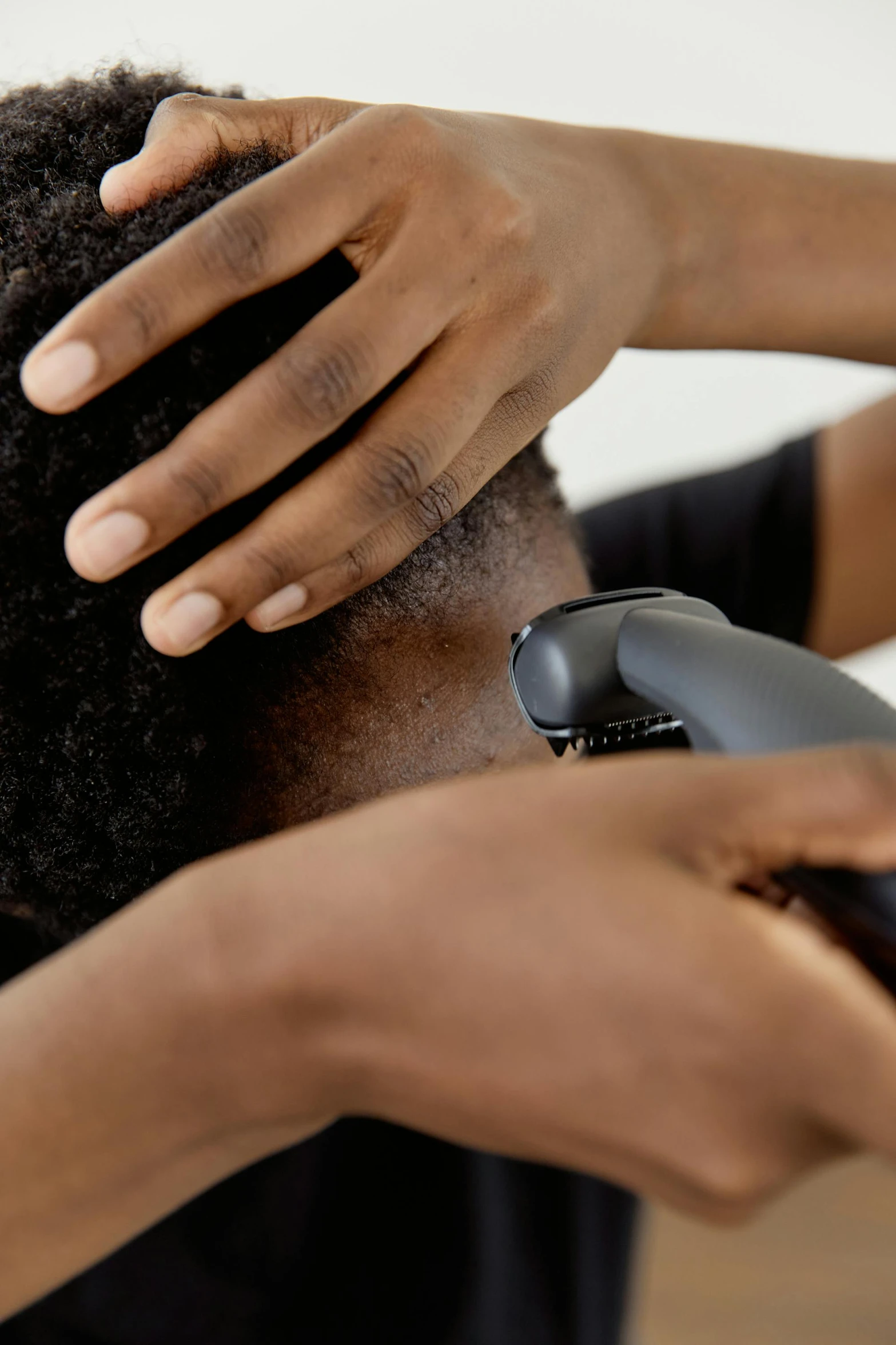a person cutting another person's hair with a hair dryer, man is with black skin, thumbnail, afar, from the side