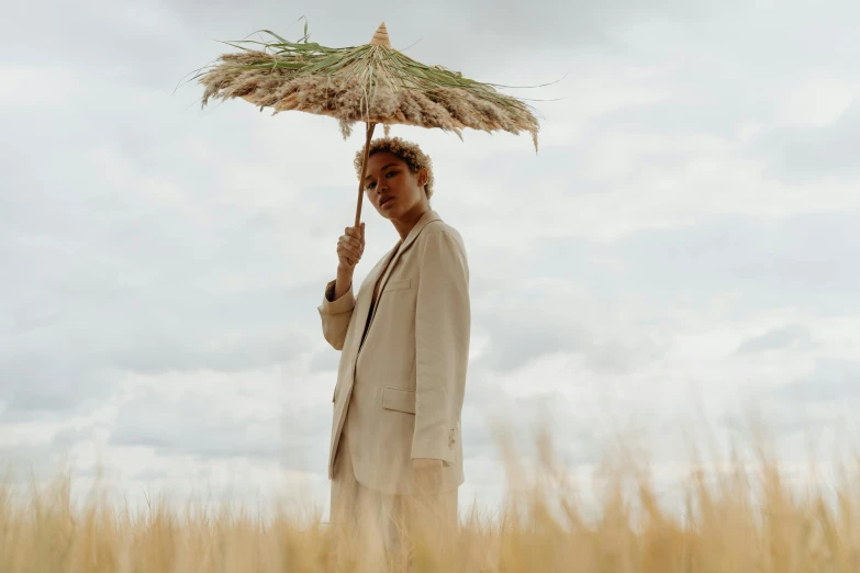 a man standing in a field holding an umbrella, ashteroth, tan suit, **cinematic, wearing hay coat